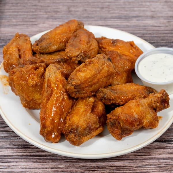 A plate of Huntington Deli & Market's golden-brown chicken wings, some coated in sauce, with a side of ranch.