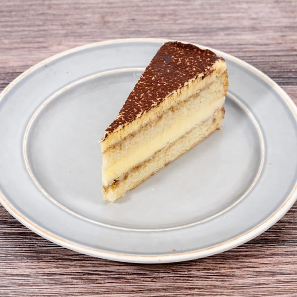 A slice of tiramisu cake with cocoa powder on top, served on a light blue plate.