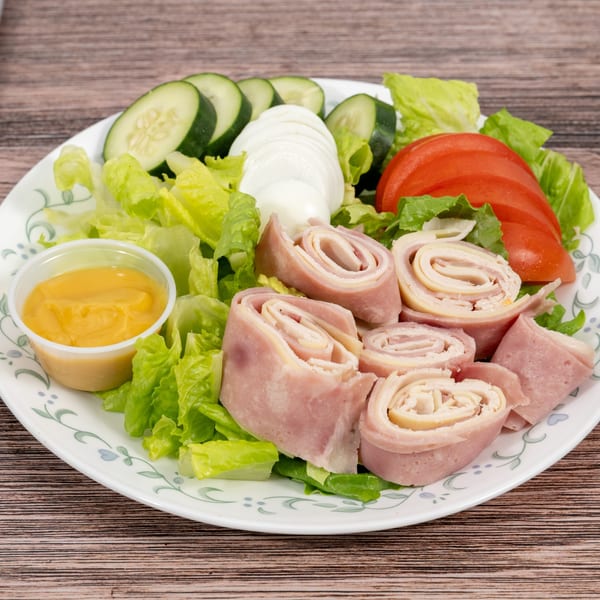 Deli salad with ham and cheese roll-ups, lettuce, cucumber, tomato, hard-boiled egg, and dressing.
