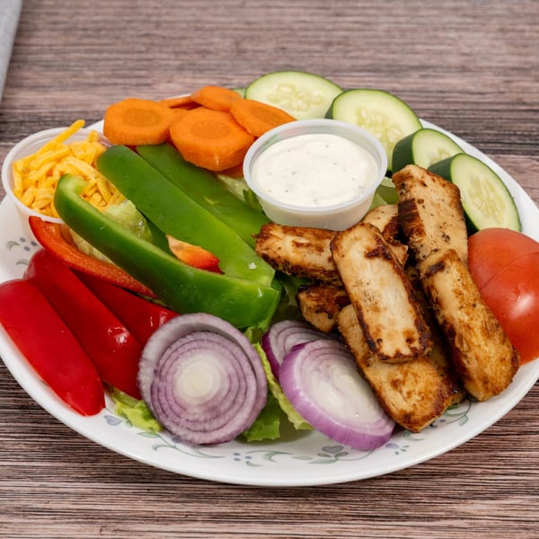 A grilled chicken salad with red onions, bell peppers, carrots, cucumbers, shredded cheese, and ranch dressing.