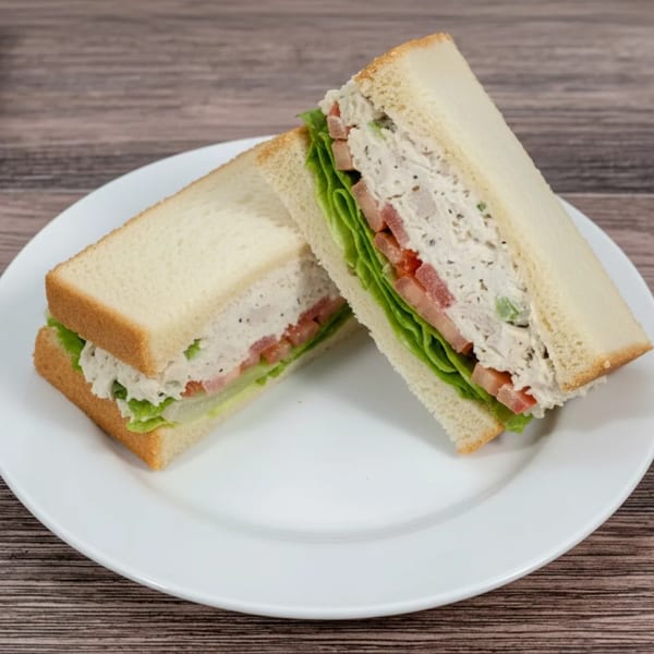 Two halves of a chicken salad sandwich with lettuce and tomato on white bread, on a white plate.