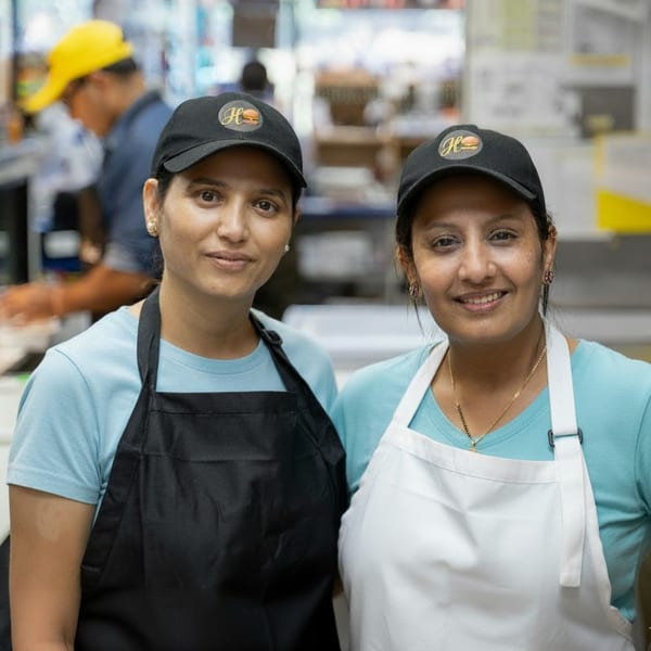 Two smiling Huntington Deli & Market employees in black and white aprons and branded caps.