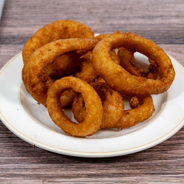 Golden-brown, crispy onion rings piled high on a white plate from Huntington Deli & Market.